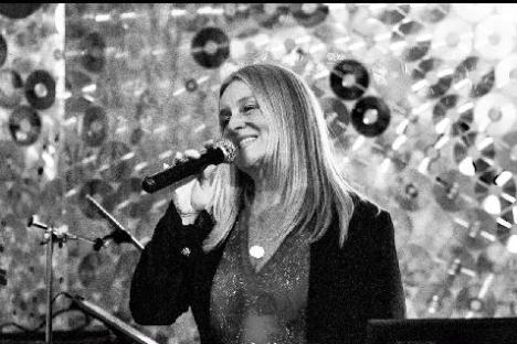 Woman singing with a microphone against a decorative backdrop.