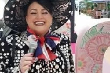Smiling person in polka dot outfit and wide-brimmed hat holding a microphone.