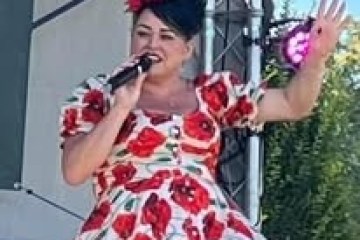Person in floral dress singing outdoors, holding a microphone.