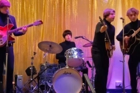 Band performing on stage with gold curtain backdrop.